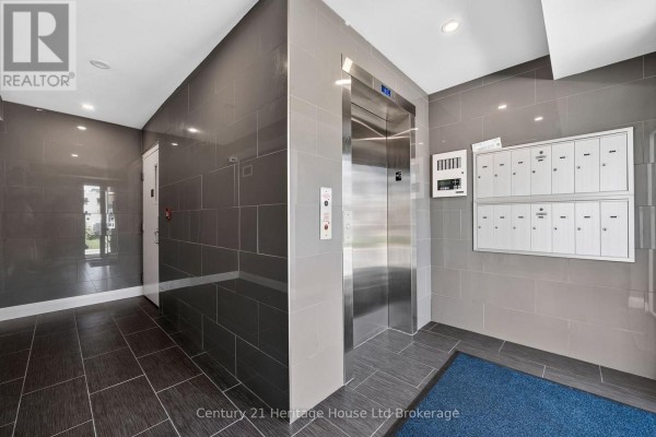 Interior hallway of an apartment building with grey tile walls, a silver elevator, and mailboxes. - 301 - 34 Brock Street, Woodstock