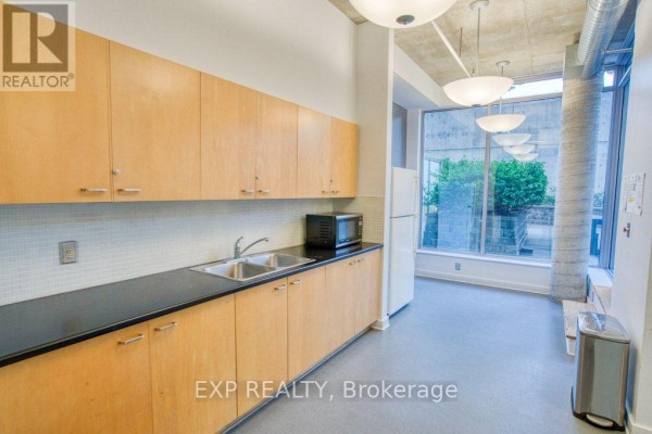 Kitchenette with light wood cabinets, black countertops, double sink, and a large window. - 301 - 383 Cumberland Street, Ottawa