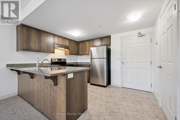 Kitchen with dark wood cabinets, granite countertops, stainless steel refrigerator, and a peninsula. - 301 - 45 Kingsbury Square, Guelph