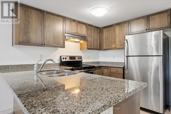 Kitchen island with granite countertop and stainless steel sink, facing dark wood cabinets and appliances. - 301 - 45 Kingsbury Square, Guelph