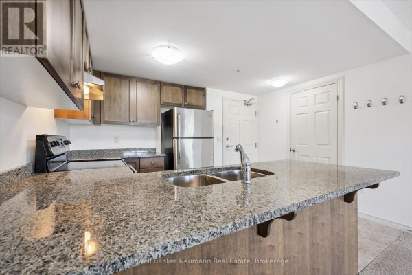 Close-up of the kitchen island with granite countertop and sink, overlooking dark wood cabinets. - 301 - 45 Kingsbury Square, Guelph