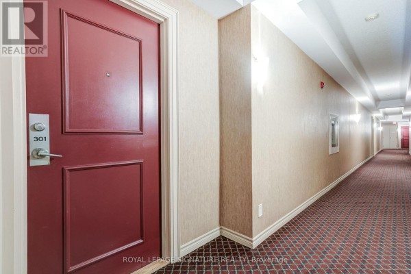 Hallway with red door 301, patterned carpet, textured walls - 301 - 483 Faith Drive Mississauga