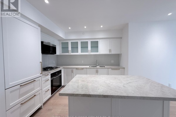 White contemporary kitchen with a grey marble island, stainless steel appliances, and glass-front cabinets. - 301 - 505 Glencairn Avenue, Toronto