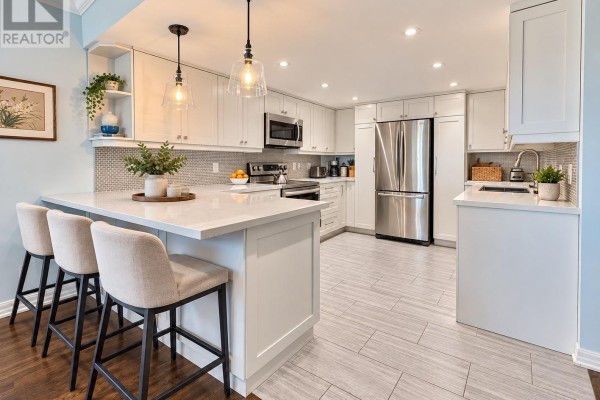 Kitchen with white cabinets, quartz countertops, island with stools, and stainless steel appliances. - 301 - 55 Carscadden Drive, Toronto
