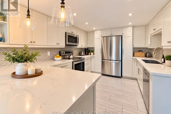 Bright kitchen with white shaker cabinets, tiled backsplash, quartz island, and stainless steel appliances. - 301 - 55 Carscadden Drive, Toronto