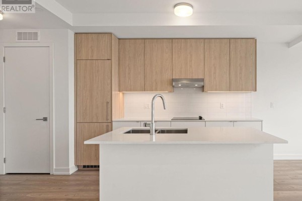 Kitchen island with a sink, white countertop, and light wood cabinetry with stainless steel appliances. - 301 - 67 Saigon Drive, Richmond Hill