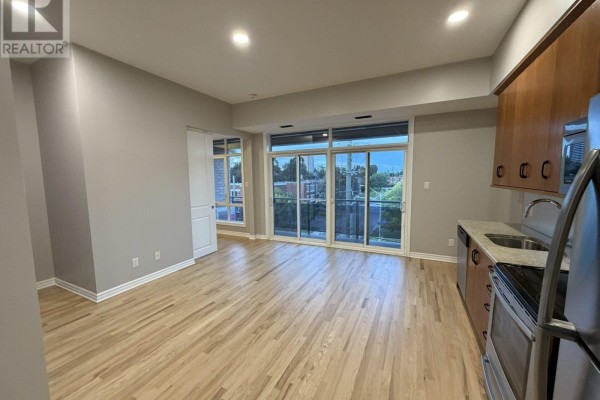 Interior view of an apartment showing living space, kitchen with stainless steel appliances, and large windows. - 301 - 682 Churchill Avenue N, Ottawa