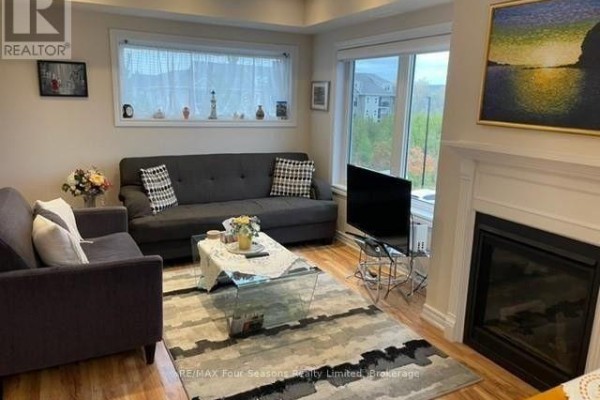 Living room with grey sofas, a glass coffee table, a fireplace, and a television. - 301 - 7 Anchorage Crescent, Collingwood