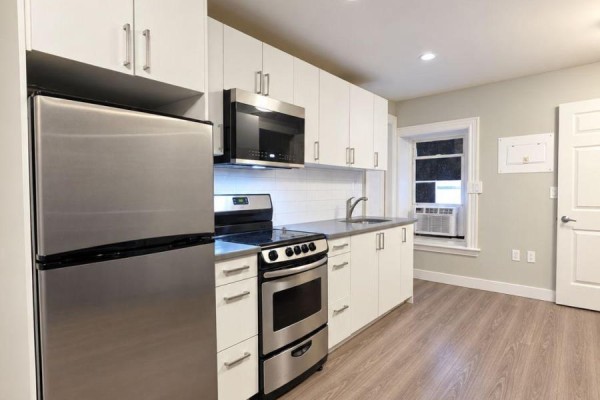 Modern kitchen with white cabinetry, stainless steel appliances, and grey laminate flooring. - 301 - 72 Victoria Avenue S, Hamilton