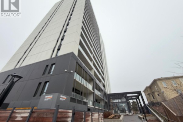 View of the apartment building's lower levels showing an entrance, garage, and adjacent older building. - 301 - 741 King Street W, Kitchener