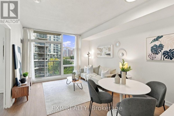 Living room with sofa, coffee table, and large window showing a city view with trees. - 301 - 9 Spadina Avenue, Toronto