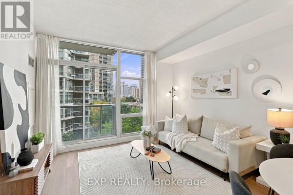 Living area with sofa, coffee table, and floor-to-ceiling window overlooking city buildings and greenery. - 301 - 9 Spadina Avenue, Toronto