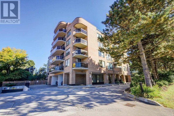 Side view of a brick apartment building with balconies and trees surrounding the property. - 301 - 96 Fifeshire Road, Toronto