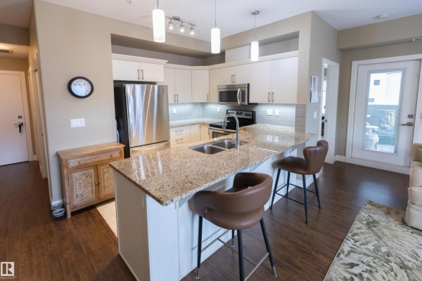 Kitchen island with granite countertop, pendant lights, stainless steel refrigerator, and bar stools. - #301 111 Festival Wy, Sherwood Park