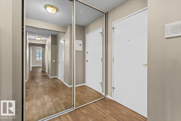 Hallway with light wood floors, mirrored closet doors, and white interior doors. - #301 11465 41 Av Nw, Edmonton