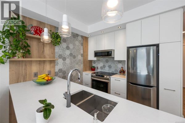 Kitchen detail with island, stainless steel sink, faucet, stainless steel appliances, and wood and tile accents. - 301 1588 North Dairy Rd, Saanich