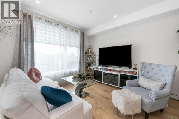 Living room with a white sofa, armchair, ottoman, glass coffee table, and large window with grey curtains. - 301 1588 North Dairy Rd, Saanich