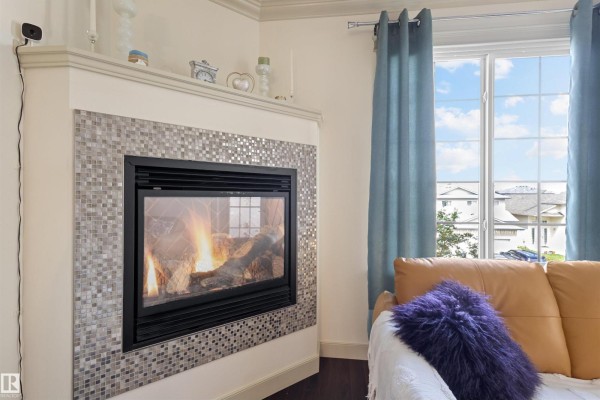 Close-up of a gas fireplace with a mosaic tile surround and a bright fire. - #301 16235 51 St Nw, Edmonton