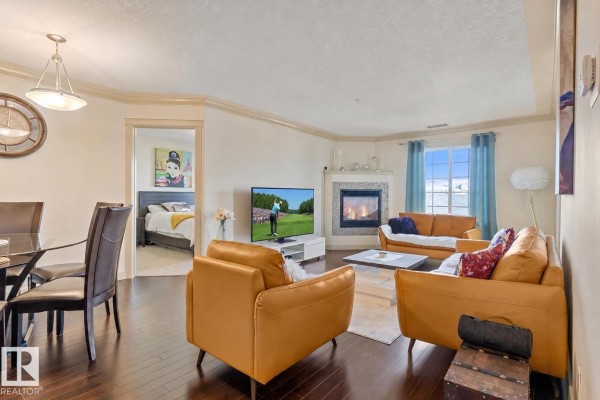 Living and dining area with a fireplace, sofa, chairs, and a view into a bedroom. - #301 16235 51 St Nw, Edmonton