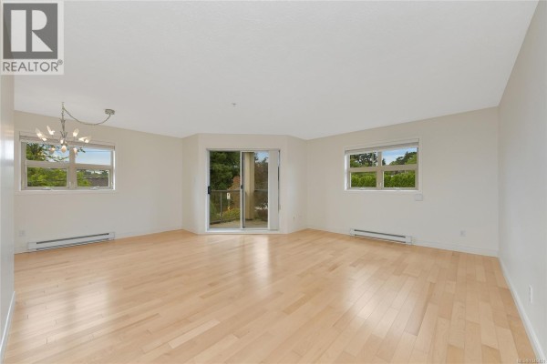 Empty living area with light wood floors and a glass sliding door leading outside. - 301 1694 Cedar Hill Cross Rd, Saanich