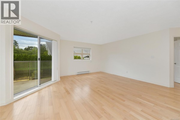 Empty living area with light wood floors, a sliding glass door, and a doorway. - 301 1694 Cedar Hill Cross Rd, Saanich