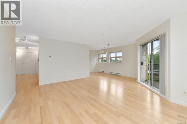 Open living area with light wood floors, a sliding glass door, and a hallway entrance. - 301 1694 Cedar Hill Cross Rd, Saanich