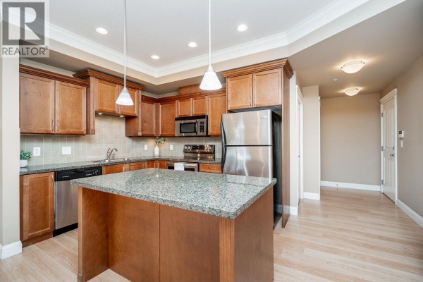 Kitchen featuring dark wood cabinets, granite countertops, stainless steel appliances, and a central island. - 301 22150 Dewdney Trunk Road, Maple Ridge