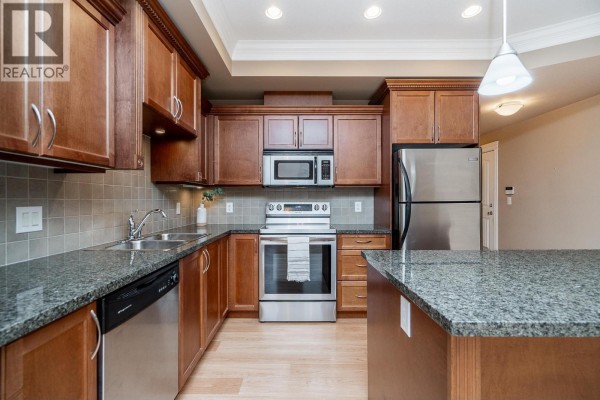 Kitchen with dark wood cabinets, granite countertops, stainless steel appliances, and a central island. - 301 22150 Dewdney Trunk Road, Maple Ridge