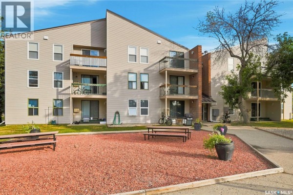 Exterior view of apartment building with balconies, grass, and red mulch landscaping with benches. - 301 34 Nollet Avenue, Regina