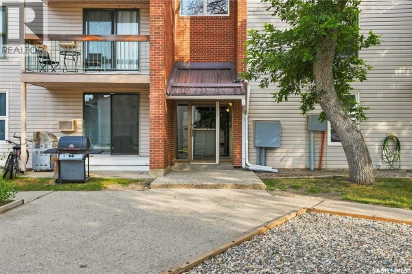 Close-up of apartment building entrance with brick pillar, metal awning, sliding door, and outdoor air conditioning unit. - 301 34 Nollet Avenue, Regina