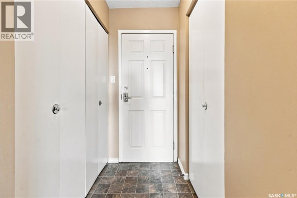 Interior hallway entrance with white bi-fold closet doors on either side and a beige front door. - 301 34 Nollet Avenue, Regina