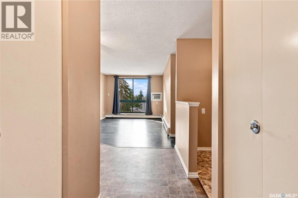 View from hallway into an empty living room with large window and view of trees. - 301 34 Nollet Avenue, Regina