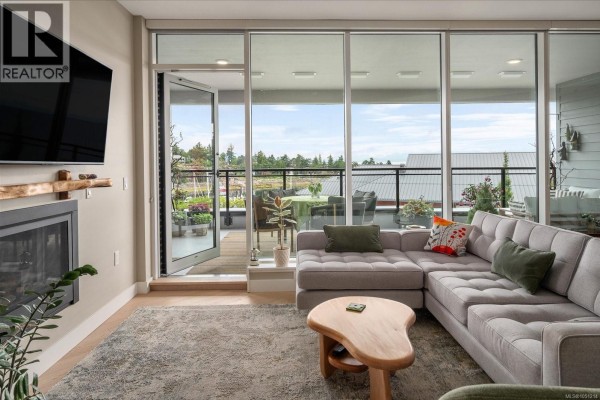 Living room with sectional sofa, fireplace, mounted TV, and glass doors opening to balcony. - 301 3529 Dolphin Dr, Nanoose Bay