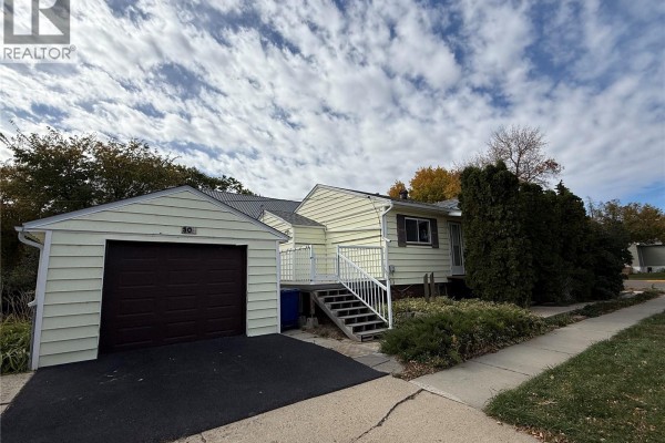 Side view of a light yellow house with a detached single-car garage and driveway. - 301 5th Avenue W, Kindersley