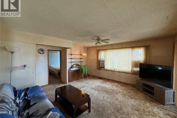 Living room with brown carpet, a couch, coffee table, television, and an opening to a bedroom. - 301 5th Avenue W, Kindersley