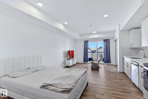 Living area with TV, large windows, and mirrored closet doors. - #301 864 Secord Bv Nw, Edmonton