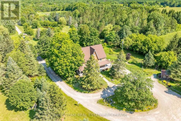 Aerial view of a brown house surrounded by mature trees and winding gravel driveways. - 301 Concession 4 Road E, Tiny