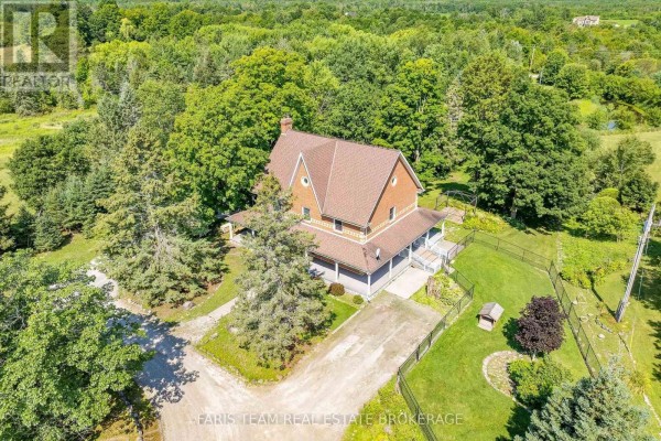Aerial view of a red brick house with a wraparound porch, surrounded by trees and fenced yards. - 301 Concession 4 Road E, Tiny