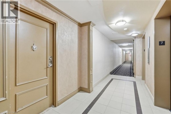 Apartment building hallway with beige walls, tiled floor, and elevators. - 301 Frances Avenue Unit# 705, Hamilton