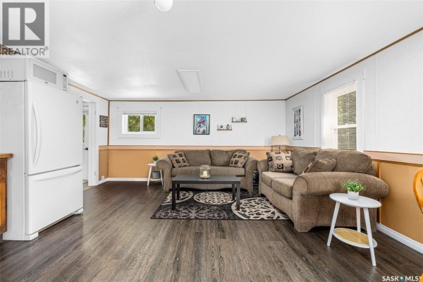 Living room with two brown sofas, a coffee table with a rug, and a white refrigerator. - 301 Pine Tree Road, Buffalo Pound Lake
