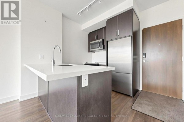 Kitchen island with a sink and dark wood cabinetry with stainless steel appliances. - Unit #415 - 301 Sea Ray Avenue, Innisfil