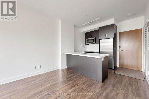 View of the kitchen area with an island and stainless steel refrigerator. - Unit #415 - 301 Sea Ray Avenue, Innisfil