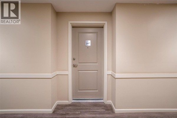 Interior hallway showing the beige front door for unit 207 with silver numbering. - 3010 35 Street Unit# 207, Vernon