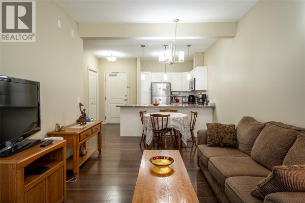 View of the living room, dining area with table, and kitchen with white cabinets. - 3010 35 Street Unit# 207, Vernon