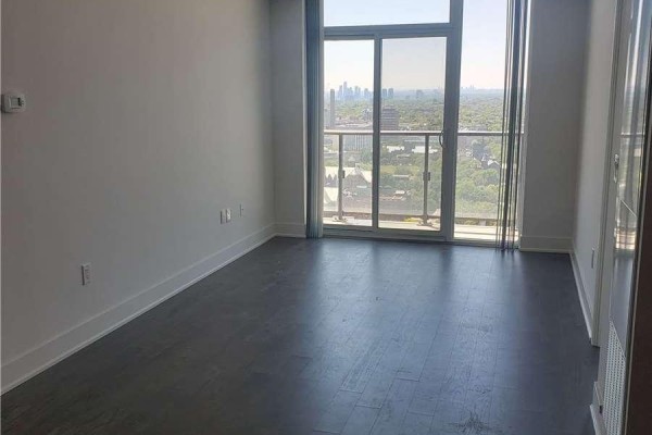 Empty living room with dark hardwood floors, white baseboards, and large windows overlooking the city. - 3012 - 955 Bay Street, Toronto