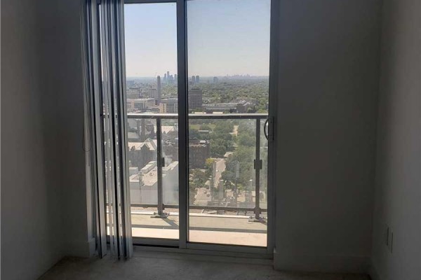 Interior view of a room with carpet, white walls, and a sliding glass door opening to a balcony with city views. - 3012 - 955 Bay Street, Toronto