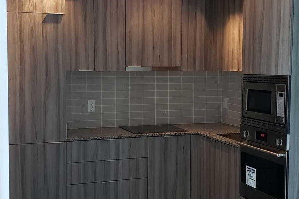 Modern kitchen with light wood cabinetry, grey tiled backsplash, granite countertops, and stainless steel appliances. - 3012 - 955 Bay Street, Toronto