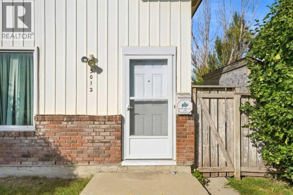 Close-up of the front door and entryway of the duplex with white siding and brick base. - 3012 Dover Crescent Se, Calgary