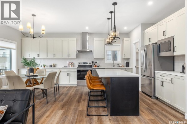 Open-concept kitchen and dining area with white cabinets, stainless steel appliances, and island seating. - 3012 Favel Drive, Regina