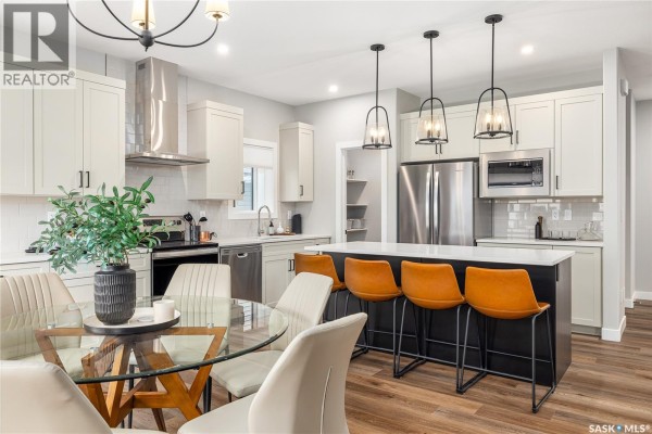 Kitchen island with orange bar stools, adjacent dining area with glass-top table and chairs. - 3012 Favel Drive, Regina